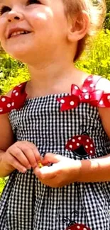 A smiling child in a checkered dress with ladybug patches, in a sunny field.