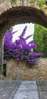 Stone archway with purple flowers in a tranquil village setting.