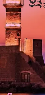 Lighthouse at sunset with pink sky and silhouette.