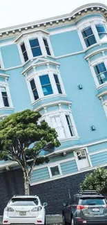 A charming blue urban house facade with detailed architecture and cars parked below.