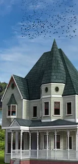 Victorian house with green roof, against blue sky and trees, ideal for wallpaper.