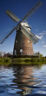 Windmill reflecting in calm water under a clear blue sky.