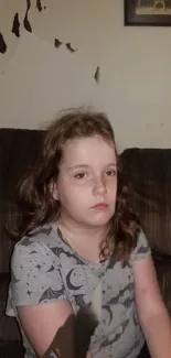 Young girl sitting on a brown sofa, looking pensive.