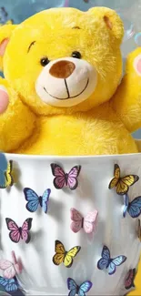 Yellow teddy bear in a butterfly-adorned cup.