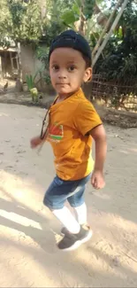 Boy in orange shirt and cap walking on a sunny path.