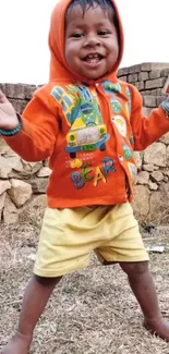 Cheerful child in orange hoodie, smiling outdoors.