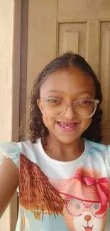 Smiling girl with glasses in front of a wooden door.