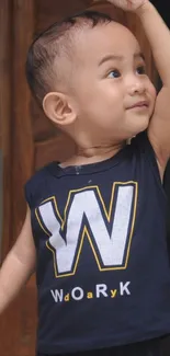 Cheerful toddler wearing navy shirt with 'W' print, raising an arm.