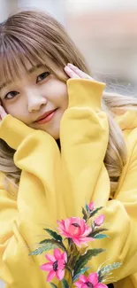 Woman in yellow hoodie smiling with pink flowers.