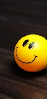 Yellow smiley face ball on dark wood background wallpaper.