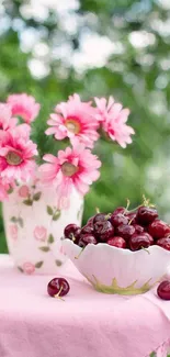 Pink flowers and cherries in bowl on tablecloth.