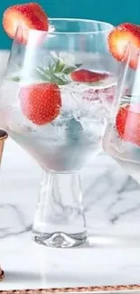 Stylish cocktail glasses with strawberries and ice on marble.