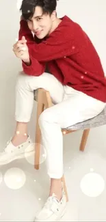 Man in a red sweater and white pants sitting on a wooden chair.