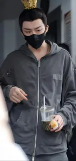 Person in gray hoodie with drink, wearing a mask.