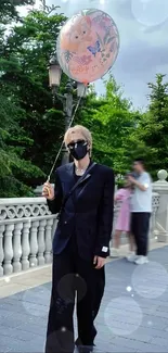 Person in black suit holding a balloon on a scenic path.