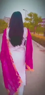 Stylish woman walking down a city path with a vibrant pink scarf.