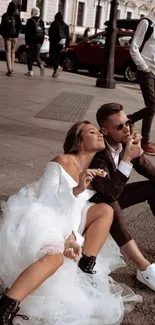 Couple in wedding attire enjoying ice cream on a city street.