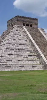 Majestic Chichen Itza pyramid under a bright blue sky with clouds and green lawn.
