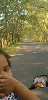 Child enjoys a ride on a tree-lined road.