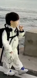 Child in white outfit by the ocean, exuding serenity.