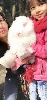 Child holding a fluffy white rabbit, dressed in a pink jacket and red scarf.