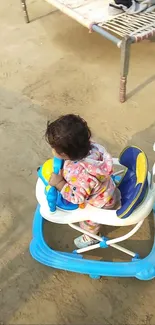 Child in a blue walker on sandy ground outdoors.