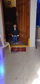 Young child stands in open doorway, indoor setting.