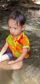 Child sitting in a colorful shirt by a serene stream in nature.