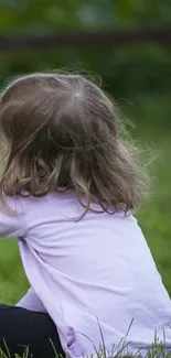 Child sitting on grass, peaceful nature scene wallpaper.