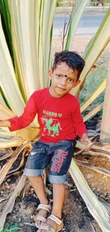 Young boy sitting in front of large green leaves.