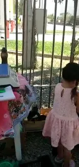 Young girl in pink dress exploring outside by a fence.