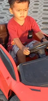 Child driving a red toy car on a sunny day.