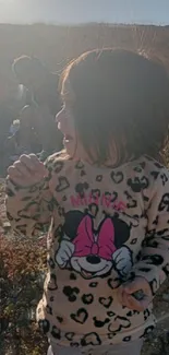 A smiling child outdoors in bright sunlight, surrounded by nature.