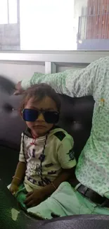 Child in sunglasses sitting on a sofa.