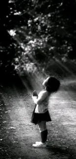 Black and white image of a child under sunrays in a forest path.