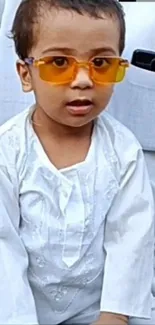 Child in white outfit with vibrant sunglasses.