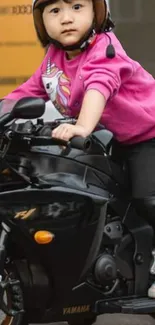 Child wearing pink hoodie on black motorcycle, looking stylish.