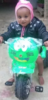 Child joyfully rides a green toy bike.