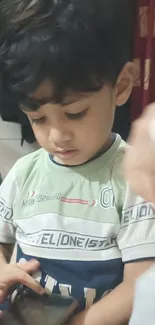 A child in a green shirt using a smartphone indoors.