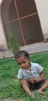 Child sitting on grass with architectural arches in the background.