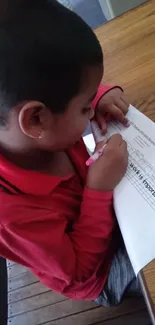 Child in red shirt writing at a desk.