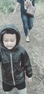 Child wearing a hooded jacket walks along a natural path with greenery.