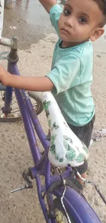 Child standing by a purple bicycle on a street.