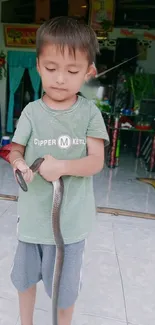 Child gently holding a snake indoors in a casual moment.