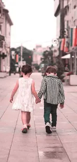 Two children walking hand in hand down a city street.