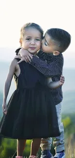 Adorable kids sharing a loving hug outdoors with a scenic mountain view.