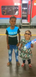 Two children smiling at a train station.