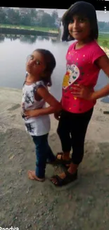 Two children happily pose by a scenic lakeside view.