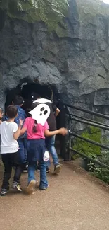 Children exploring a cave entrance with greenery and rocky textures.