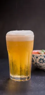 Glass of chilled beer with a patterned bowl on dark background.